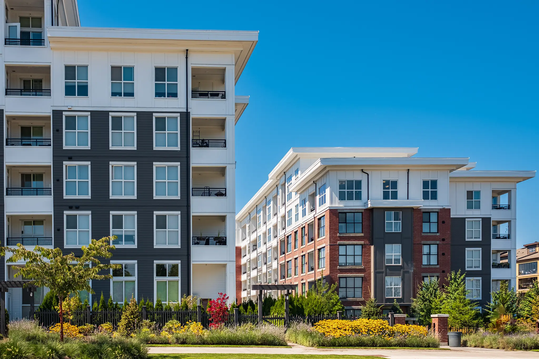 Modern apartment buildings with contrasting facades, surrounded by vibrant landscaping and a clear blue sky.